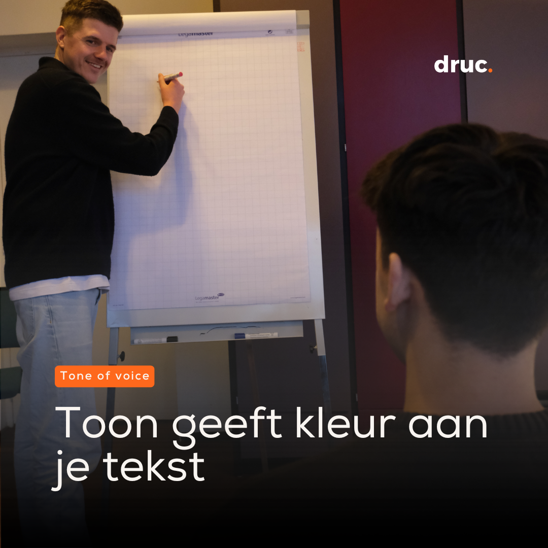 Man staat glimlachend met een stift bij een flip-over tijdens een presentatie aan een collega.