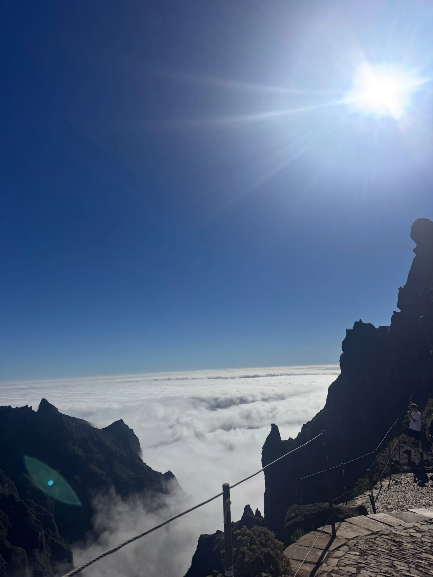 Bergpad op Madeira met uitzicht over een wit wolkendek onder een felle zon en helderblauwe lucht.