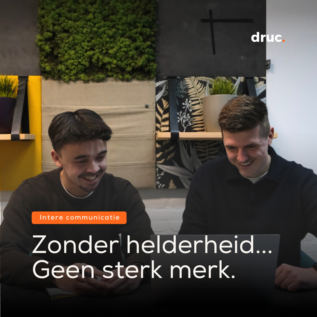 Twee lachende jonge mannen overleggen achter een laptop in een kantoorruimte.